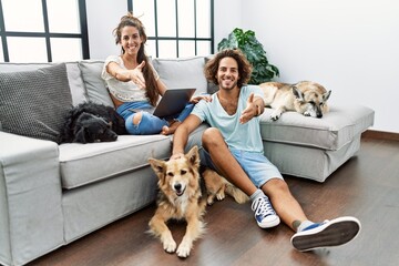 Young hispanic couple with dogs relaxing at home smiling friendly offering handshake as greeting and welcoming. successful business.