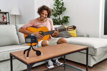 Young hispanic man recording with camera playing classical guitar at home.