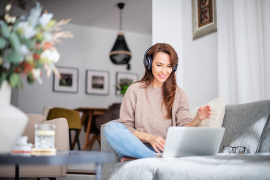Beautiful woman at home sitting on the sofa while using laptop and headphone