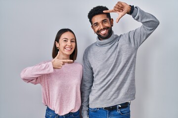 Fototapeta premium Young hispanic couple standing together smiling making frame with hands and fingers with happy face. creativity and photography concept.