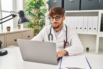 Young arab man wearing doctor uniform using laptop working at clinic