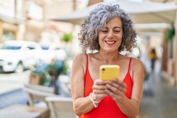 Middle age grey-haired woman smiling confident using smartphone at street