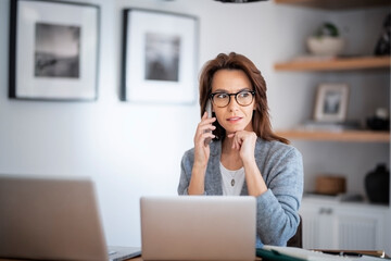 Serious faced woman having a call and using laptop while working from home