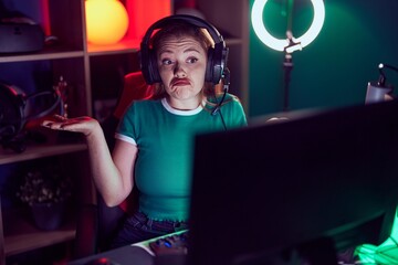 Redhead woman playing video games clueless and confused expression with arms and hands raised. doubt concept. © Krakenimages.com