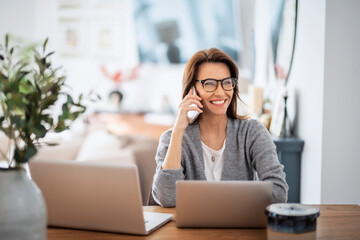 Business woman using mobile phone in front of laptops while working from home