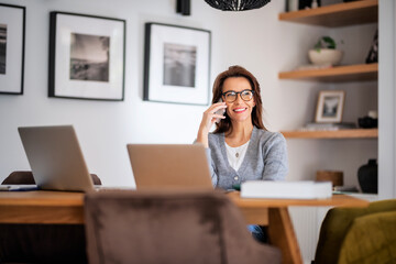 Business woman using mobile phone in front of laptops while working from home