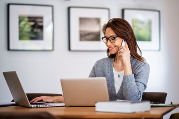 Businesswoman using mobile phone in front of laptop while working from home