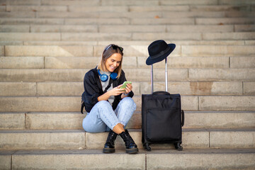 Full body woman sitting on stairs with suitcase and mobile phone