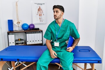 Young physiotherapist man working at pain recovery clinic looking to side, relax profile pose with...