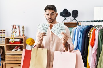 Young hispanic man holding shopping bags and dollars at retail shop skeptic and nervous, frowning upset because of problem. negative person.