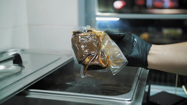 Cooking Meat In A Vacuum Using Sous-vide Technology. Hand Holding Meat Ribs In Sous Vide Bag, Under Special Machine, In A Restaurant. Cooking In Modern Kitchen.