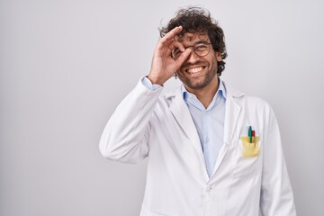 Hispanic young man wearing doctor uniform doing ok gesture with hand smiling, eye looking through fingers with happy face.