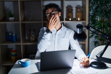 Hispanic man working at the office at night bored yawning tired covering mouth with hand. restless and sleepiness.