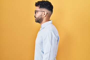 Hispanic man with beard standing over yellow background looking to side, relax profile pose with...
