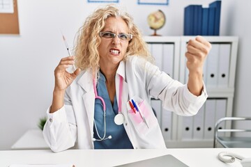 Middle age doctor woman holding syringe at the clinic annoyed and frustrated shouting with anger,...