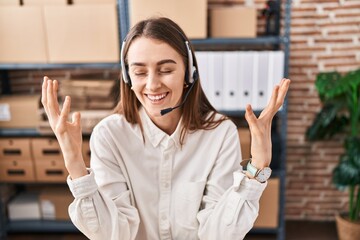 Young caucasian woman working at small business ecommerce wearing headset celebrating mad and crazy for success with arms raised and closed eyes screaming excited. winner concept