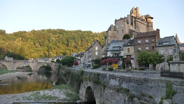 Summer view of scenic French township of Estaing on bank of Lot River overlooking medieval stone arched bridge and fortified castle towering above residential buildings. High quality 4k footage