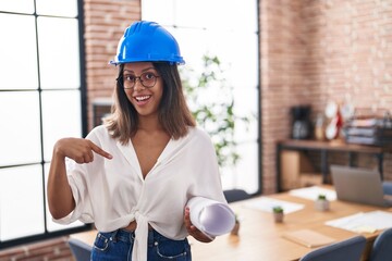 Hispanic young woman wearing architect hardhat at office pointing finger to one self smiling happy and proud