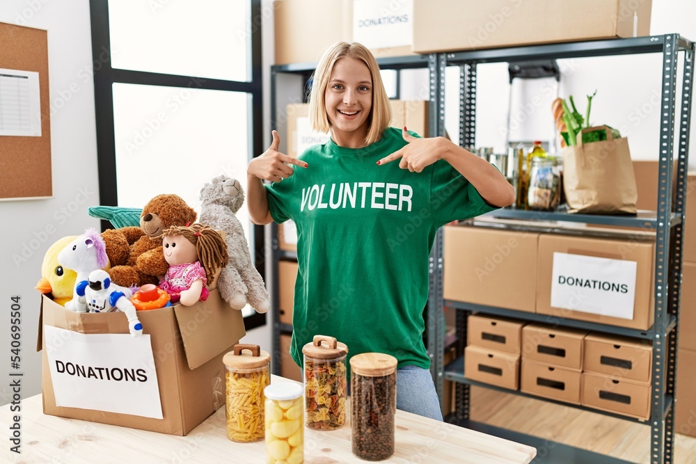 Sticker Young caucasian woman wearing volunteer t shirt at donations stand looking confident with smile on face, pointing oneself with fingers proud and happy.