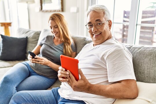 Middle age hispanic couple smiling happy using tablet and smartphone at home.