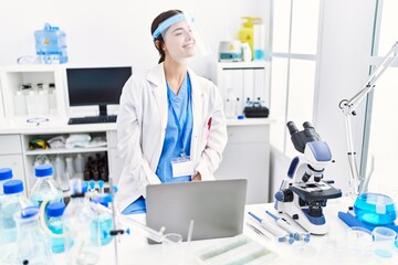 Young hispanic woman wearing scientist uniform looking away to side with smile on face, natural expression. laughing confident.