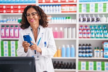 Middle age woman pharmacist using smartphone working at pharmacy