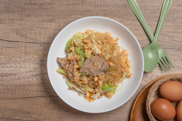 Stir fried vermicelli with pork, egg and collard greens in a white plate.
