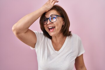 Middle age hispanic woman standing over pink background surprised with hand on head for mistake, remember error. forgot, bad memory concept.