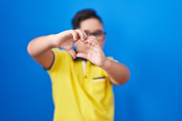 Young hispanic kid standing over blue background smiling in love showing heart symbol and shape with hands. romantic concept.