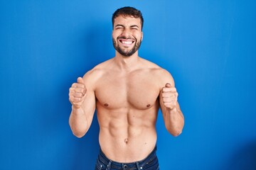 Fototapeta premium Handsome hispanic man standing shirtless excited for success with arms raised and eyes closed celebrating victory smiling. winner concept.