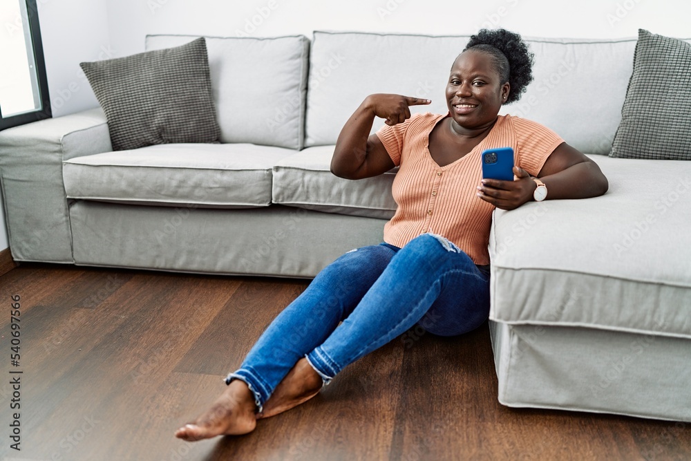 Sticker Young african woman using smartphone sitting on the floor at home smiling cheerful showing and pointing with fingers teeth and mouth. dental health concept.