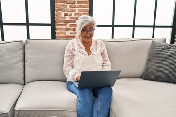 Middle age woman using laptop sitting on sofa at home