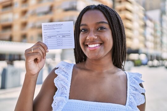Young african american girl smiling happy holding covid-19 vaccination record card at the city.