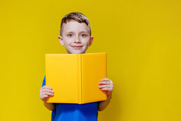 Positive preschool boy in an blueT-shirt holding an open yellow copybook on yellow background