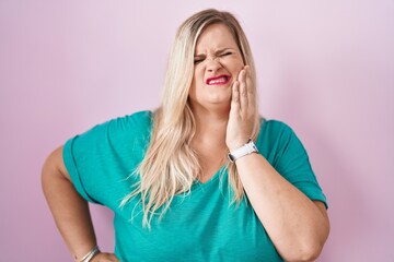 Caucasian plus size woman standing over pink background touching mouth with hand with painful expression because of toothache or dental illness on teeth. dentist