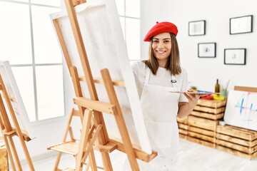Young hispanic artist woman wearing french beret drawing at art studio.
