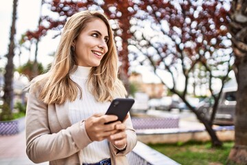 Young blonde woman smiling confident using smartphone at park