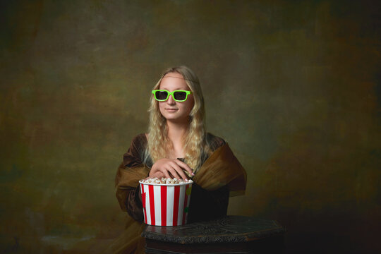 At movie. Elegant young girl with long blonde hair wearing medieval dress like Mona Lisa replica over dark vintage background. Vintage style, art, fashion, comparison of eras concept.