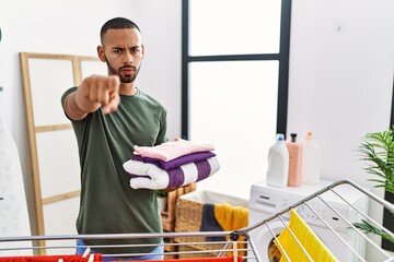 African american man holding folded laundry from clothline pointing with finger to the camera and to you, confident gesture looking serious