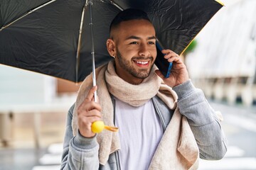 African american man talking on smartphone holding umbrella at street