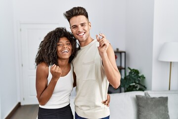 Young interracial couple holding keys of new home screaming proud, celebrating victory and success...