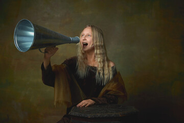 Beautiful young girl with long blonde hair wearing medieval dress shouting at megaphone over dark vintage background. Retro style, art, fashion, comparison of eras concept.