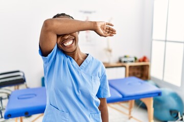 Obraz premium Black woman with braids working at pain recovery clinic covering eyes with arm smiling cheerful and funny. blind concept.