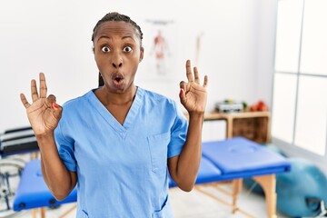 Black woman with braids working at pain recovery clinic looking surprised and shocked doing ok...