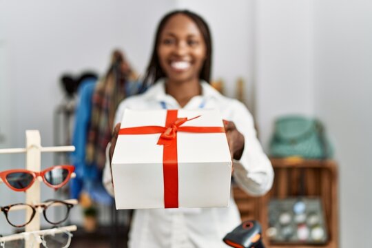 Young african american shopkeeper woman smiling happy holding gift at clothing store.