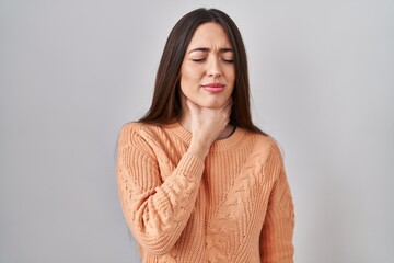 Young brunette woman standing over white background touching painful neck, sore throat for flu,...