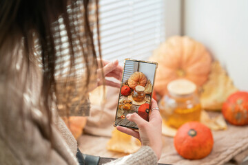 Girl taking photo of pumpkins, autumn leaves and teapot on a window. Girl photographing on phone rustic halloween composition. Happy Thanksgiving and Halloween