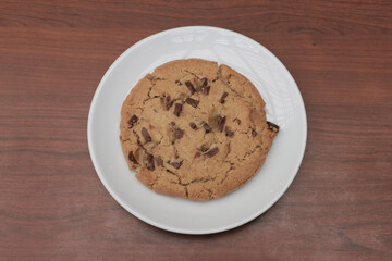 Big American chocolate chip cookie on white plate on wooden table