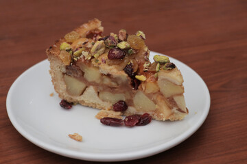 Apple pie on a white plate on a wooden table topped with pistacio nuts