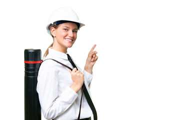 Young architect caucasian woman with helmet and holding blueprints over isolated background pointing finger to the side and presenting a product - obrazy, fototapety, plakaty